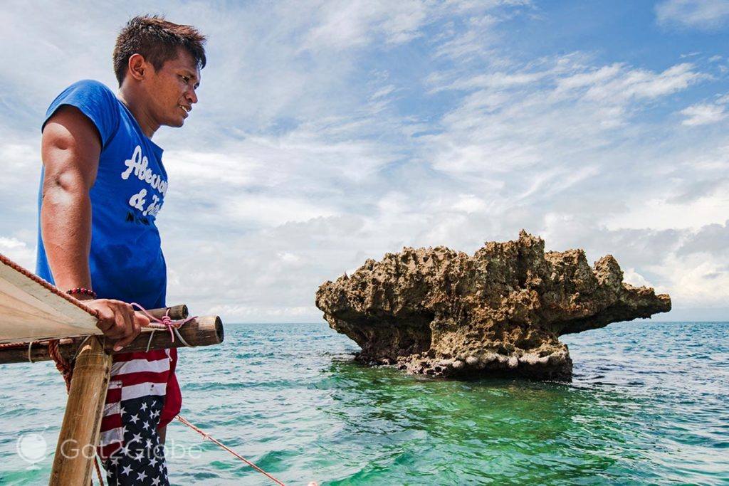 Timoneiro de uma bangka junto a um rochedo nas imediações da ilha Ave Maria