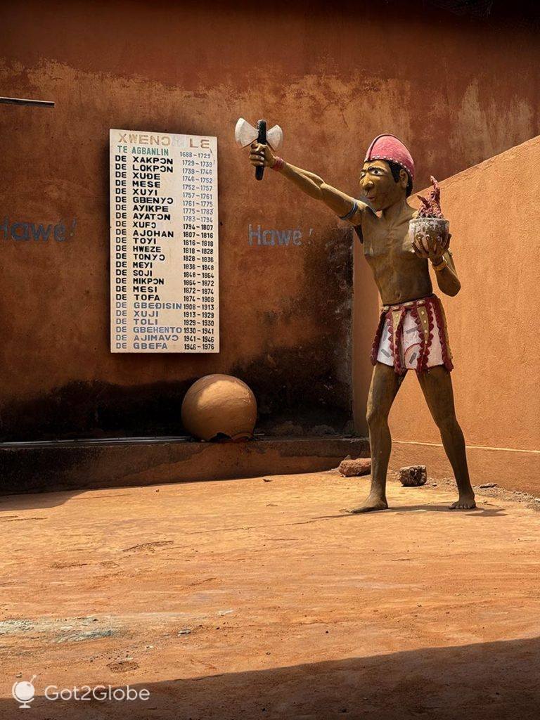Boneco anima um espaço do palácio real que exibe uma lista dos reis de Porto Novo