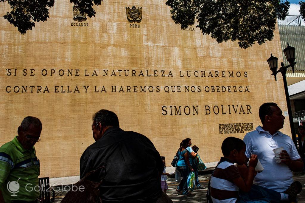 Vultos em frente a um mural próximo da Plaza Bolívar que exibe uma citação de Simón Bolívar
