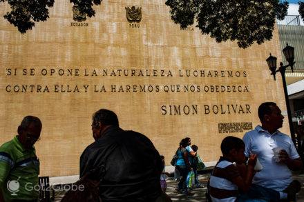 Vultos em frente a um mural próximo da Plaza Bolívar que exibe uma citação de Simón Bolívar