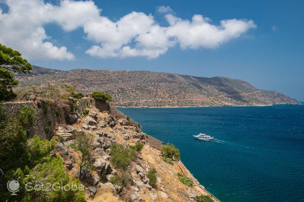 Barco navega ao largo do litoral ocidental de Spinalonga
