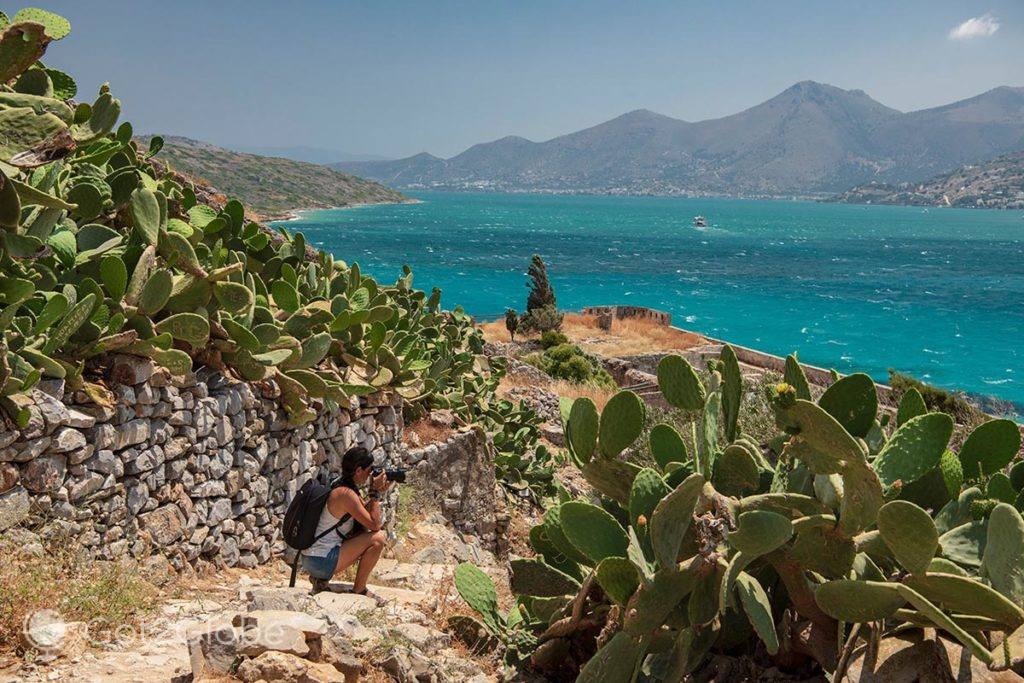 Visitante fotografa num caminho murado e repleto de cactos de Spinalonga.